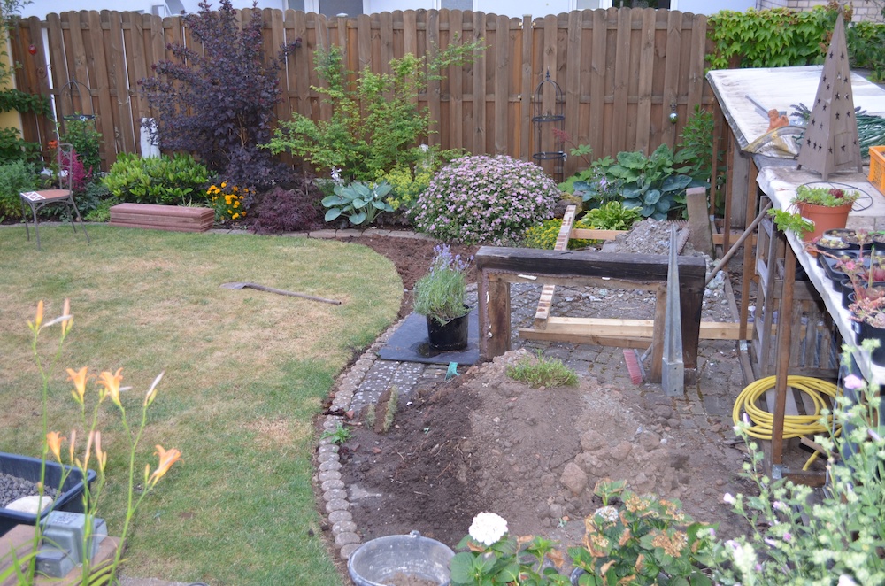 Hier Blick von der Terrasse auf das Vorhaben. Hier sieht man, daß das Holzlager um ca. 100cm mehr in die Wiese ragt, als die später geplante Aussenküche. Vorm Holzlager wird die Bepflanzung geändert. Das sind die einzigen Flächen mit etwas Schatten hier werden wieder Hosta, Funkie und Schaublatt hingepflanzt.
