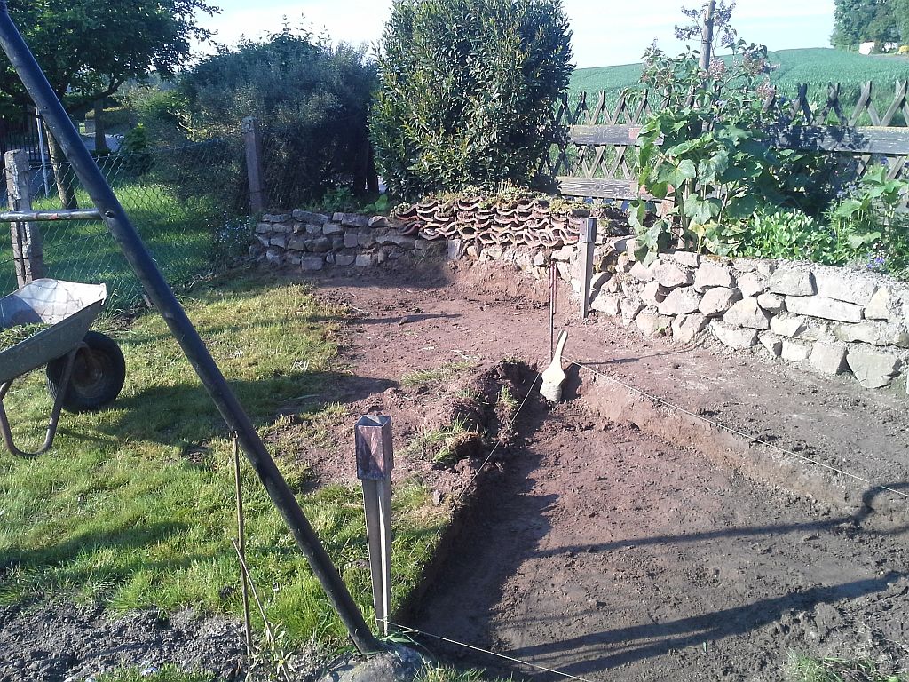 Hier noch eine Natursteinmauer und aus Ziegeln ein Insektenhotel . Im Vordergrund wird das Fundament für das Backhaus ausgehoben